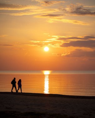 Güzel bir yaz günbatımı manzarası. Sahilde yürüyen siluetler, Baltık Denizi 'nin kostüm çizgisinin keyfini çıkarıyorlar. Letonya, Avrupa 'nın akşam manzarası.