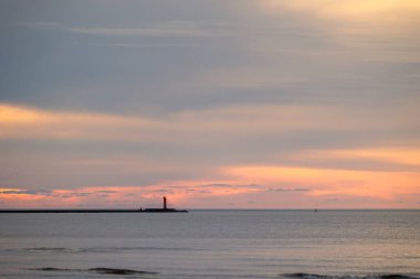 Güzel bir gün batımı manzarası. Uzakta küçük bir deniz feneri var. Renkli akşam gökyüzüne karşı. Riga, Letonya 'da yaz akşamı.