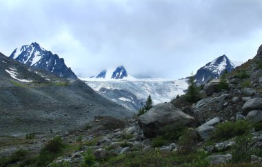 Sofya buzulu yazın Altai 'de yüksek bir dağ geçidinde, büyük taşlı bir yamacın önünde, buzulun üzerinde kar, kayalık yamaçlar, bulutlu gökyüzü ve üç keskin tepe vardır.