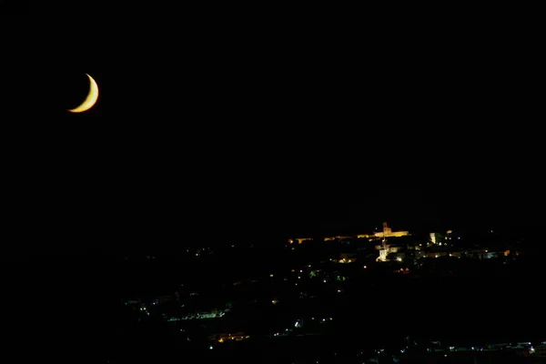 病态的月亮 在山丘上一个小镇的夜灯中 开始向着夕阳升起 — 图库照片
