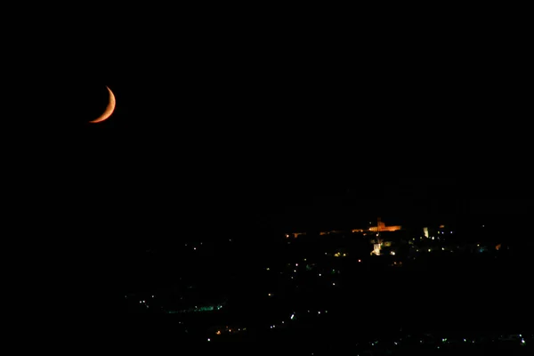 病态的月亮 在山丘上一个小镇的夜灯中 开始向着夕阳升起 — 图库照片
