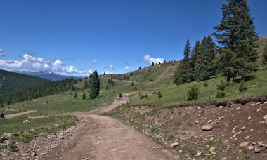 Uzaktaki kırmızı ATV bir dağ patikasının çamur birikintileri boyunca ilerliyor.