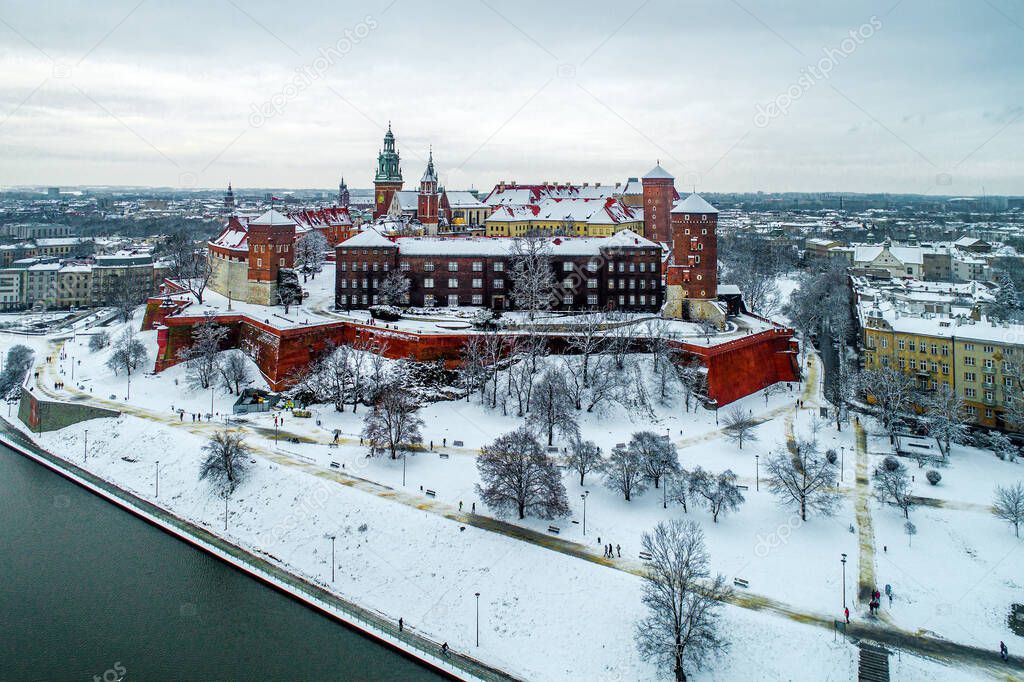 Historic royal Wawel Castle and Cathedral in Cracow, Poland, with Vistula River, walking people, snow and promenade in winter