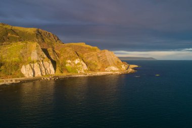 Kuzey İrlanda, İngiltere. Atlantik kıyısı. Cliffs ve Causeway Coastal Route. Avrupa 'nın en manzaralı kıyı yollarından biri. Güneş doğarken Garron Point yakınlarında kara fırtınalı bulutlarla hava manzarası