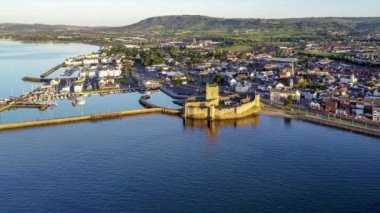 Ortaçağ Norman Kalesi ve Carrickfergus Limanı. Gün doğumunda Belfast yakınlarında. Marina, yat dalgaları ve kasabayla birlikte 4K hava aracı yaklaşıyor.