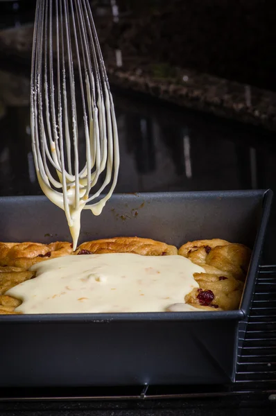 Pouring icing on fresh cinnamon rolls — Stock Photo, Image