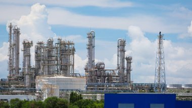 Karmaşık mühendislik yapılarına ve damıtma kulelerine sahip modern bir petrol rafinerisi ve kimya fabrikasının manzara görüntüsü parlak mavi gökyüzüne karşıdır, teknoloji ve endüstriyel ilerlemeyi sembolize eder..