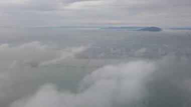 Alçak bulutların üzerinde uçan bir hava. Arkaplan, Butterworth konteynır terminali.