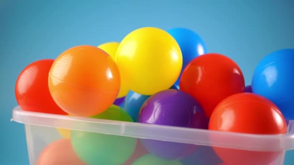 在蓝色背景下旋转的容器中的许多彩色塑料球 — 图库视频影像
