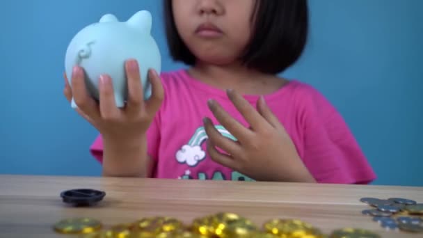 小さな中国の女の子は 貯金箱からコインを手に入れようとします 前景はビットコイン — ストック動画