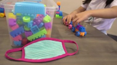 Küçük kız maskeyi masaya koy ve tuğla oyunu oyna.