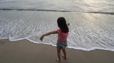 Yavaş hareket eden, çıplak ayaklı, yüz maskeli küçük kız sahildeki yumuşak deniz dalgalarının tadını çıkar.