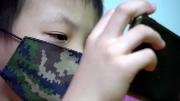 亚洲男孩戴着士兵伪装的彩色面具 玩智能手机 — 图库视频影像
