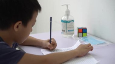 ASean Çinli çocuk okul ödevi yapıyor. Masada yeni bir yüz maskesi ve dezenfektan normal.