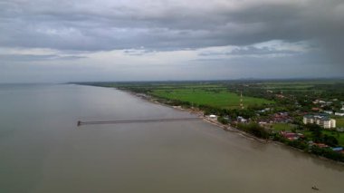 Arka planda bir kasaba olan bir plaj manzarası. Su açık mavi bir renktir. Gökyüzü görüntüsü Yan, Kedah