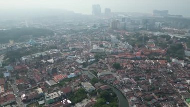 İçinden nehir akan bir şehir. Binalar yüksek ve gökyüzü bulutlu. Yolda bir sürü araba var. Hava sisli görünümü Melaka