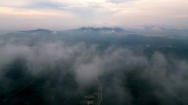 Gökyüzünde bulutlar olan bir dağ sırası uzaklıktan görülebilir. Bulutlar alçak ve yoğun, gökyüzünü kaplıyor. Hava balıkçı köyü Sungai Ayam, Batu Pahat