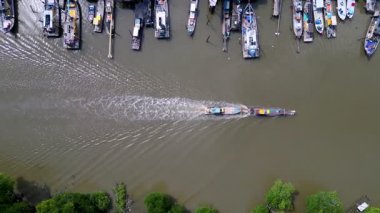 Bir tekne nehirde seyahat ediyor. Arka planda bir sürü tekne var. Su kahverengi ve bulanık. Hava Kuala Sepetang Kasabası