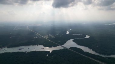 Uzakta önplanda köprüsü olan bir nehir gösterilir. Gökyüzü bulutlu ve güneş bulutların arasında parlıyor. Kong Kong 'da hava manzaralı gece gün batımı, Johor
