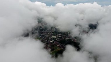 Yoğun bir bulut tabakasının arasından bir şehir görülebilir. Bulutlar alçak ve yoğundur, gökyüzünü kaplar ve kasvetli bir atmosfer yaratır.
