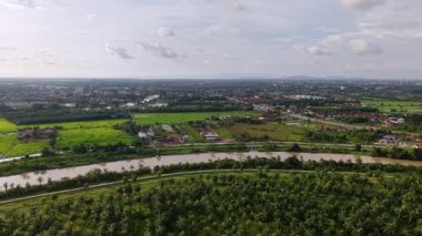 İçinden bir nehir akan yemyeşil bir arazi. Gökyüzü bulutlu ve şehir arka planda.