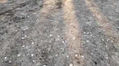 Bir sürü küçük deliği olan gri beton bir zemin. Delikler kir ve molozla dolu. Zemin bir toz tabakasıyla kaplı.