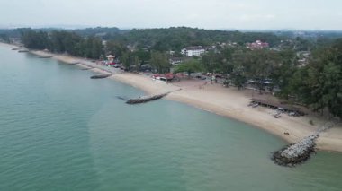 Kayalık bir kıyı şeridi ve birkaç bina olan bir sahil. Su sakin ve mavidir. Hava Tankong Kling, Melaka