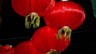 Siyah arka planda asılı kırmızı fenerler. Fenerler kırmızı ve altın kaplama. Toplamda dört fener var.