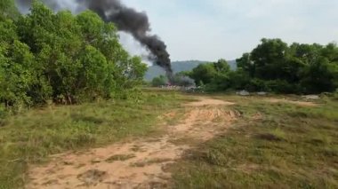 Ormanda bir ateş yanıyor. Duman siyah ve dalgalı. Yangın bir tarlanın ortasında.