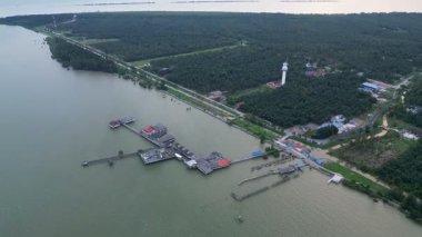 İskelesi ve deniz feneri olan bir su manzarası. Su yeşil ve iskele kırmızıdır. Aerial Tanjung Piai, johor