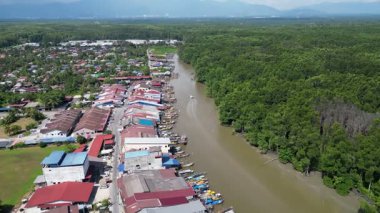 Bir nehir evleri ve tekneleri olan bir kasabadan geçiyor. Nehir kahverengi ve evler kırmızıdır. Hava Kuala Sepetang Kasabası
