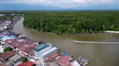 Kasabanın yakınındaki bir nehirde bir tekne seyahat ediyor. Nehir kahverengidir ve tekne beyazdır. Hava Kuala Sepetang balıkçı köyü