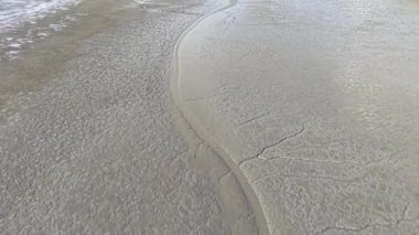 İnsansız hava aracı görüntüsü gelgit çamurlu ve çamurlu kıyı şeridini kanallar, dalgalar ve çatlak çökeltilerle gösteriyor.