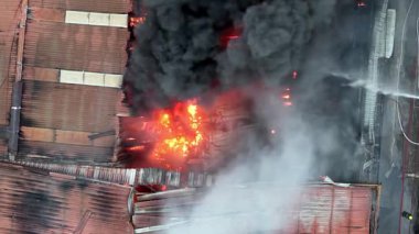 Hava manzaralı bir binada yangın var ve itfaiyeciler söndürmeye çalışıyor. Bina alevler içinde ve duman dışarı yükseliyor.