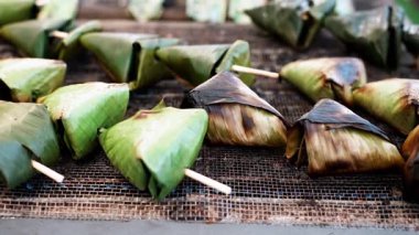 Muz yapraklarına sarılı sata balık kekleri tel örgülü sokak yemekleri tezgahında ızgara yapıyor..