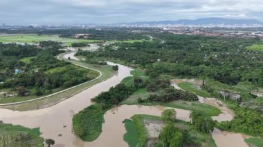Labuh Banting nehrinin drone görüntüsü dolambaçlı kanallar, sulak alanlar, palmiye bitkileri ve uzak şehir silueti.