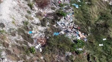 Çimenli yamaçta, karışık ev eşyaları, inşaat atıkları ve plastik atıkların bulunduğu yasadışı atık alanının hava manzarası.