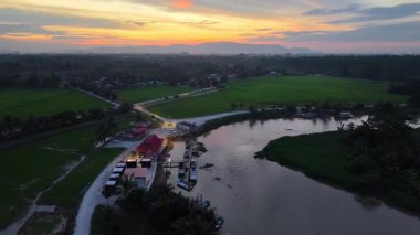 Labuh Banting Nehri İskelesi, tekneler, yollar ve alacakaranlıktaki pirinç tarlalarının hava aracı görüntüsü..
