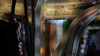 Arabaları ve arka planda köprüsü olan bir şehir caddesi. Sokaklar geceleri aydınlık.