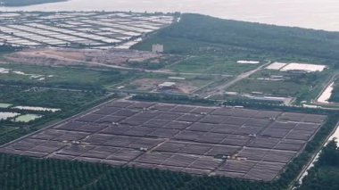 Yukarıdan aşağıya bakan insansız hava aracı perspektifi tarım arazisi ve kıyı göletlerine komşu geniş açık güneş paneli çiftliklerini gösteriyor