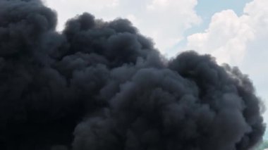 Black cloud filled with smoke is in the sky. The sky is mostly clear with a few clouds scattered around