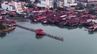 George Town, Penang, Malezya - Ağustos 07 2025: Penang 'deki Tan Jetty' deki kırmızı ahşap evin havadan görünüşü kıyı sularına karşı parlayan durgun miras mimarisini gösteriyor