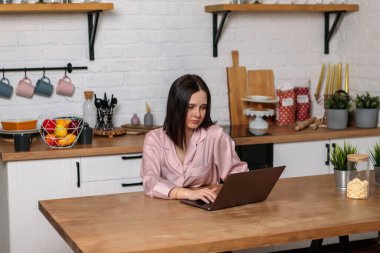 Ofiste çalışan bir kadın mutfaktan uzakta, bilgisayarın başında oturuyor. Çevrimiçi eğitim ve çalışma mesafesi. Kız öğrenci sınavlara hazırlanıyor..