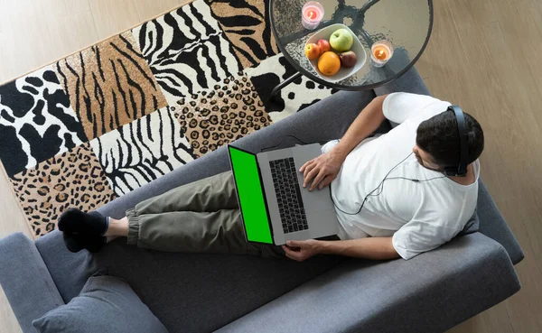 Man lies on a sofa and works on a laptop in a modern loft house. Top down view
