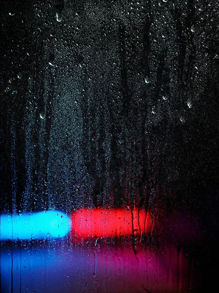 Window and water drops, emergency lights on background