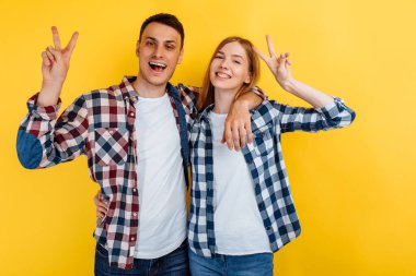 Mutlu genç arkadaşlar, erkek ve kadın, sarı arka planda barış jesti gösteriyorlar.