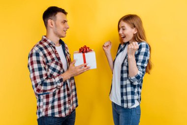 Birbirine aşık genç bir çift sarı arka planda hediye kutusunu tutuyor, Sevgililer Günü 'nde.