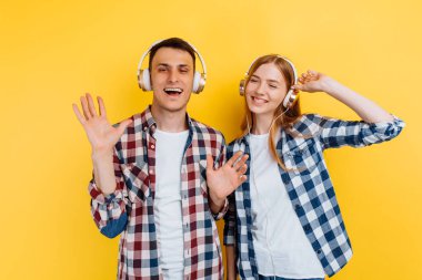Genç ve güzel arkadaşlar, erkek ve kadın sarı arka planda kulaklıkla müzik dinliyorlar.
