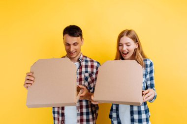 Sarı arka planda pizza kutuları olan neşeli genç arkadaşlar.