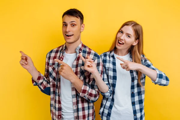 幸せな若いカップル 男と女 黄色の背景に隔離されたコピースペースで指で指して — ストック写真